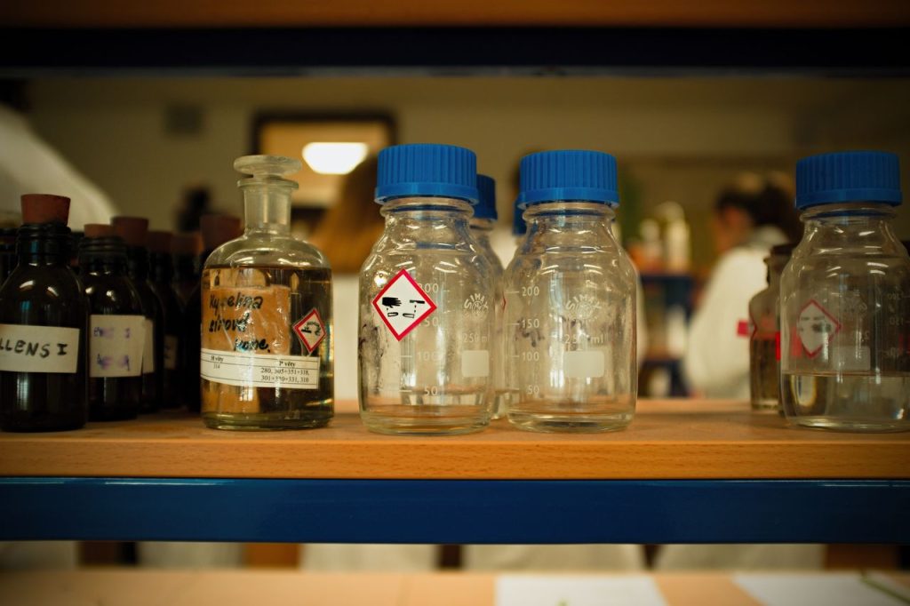 Close-up view of glass bottles and containers on a laboratory shelf with chemical symbols.